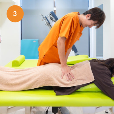 ベッドにうつ伏せになった患者の背中に軽く触れ、体の状態を確認するスタッフ。