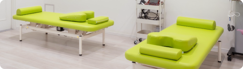 光が差し込む施術スペースに整然と配置された緑の施術ベッド。